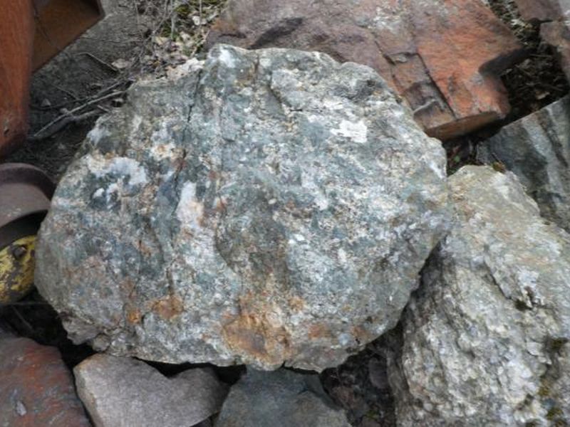 Grey-green rock with pale mineral flecks, resting on rusted mine equipment.